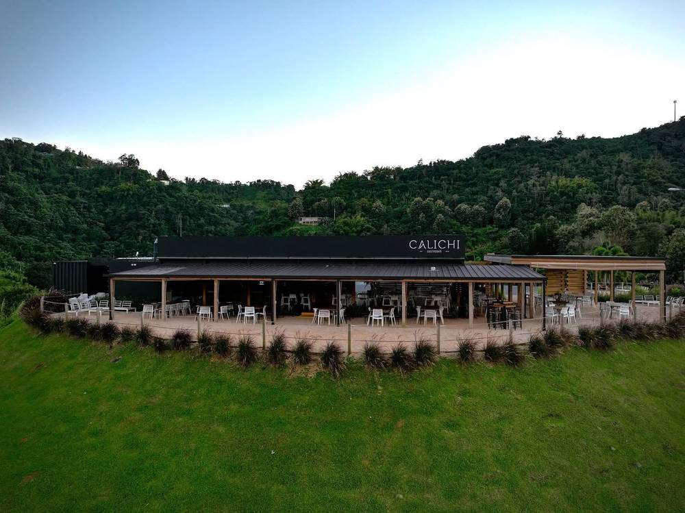 Calichi Gastrobar at dusk: a long open-air dining pavilion set into the green hillside, with the lit sign above the terrace