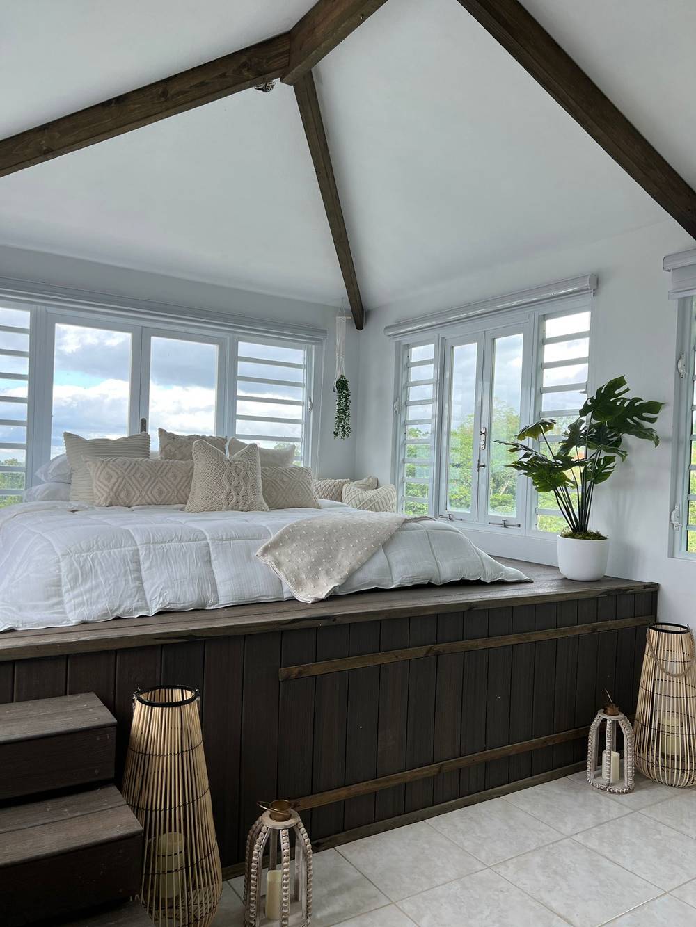 A bed set into a raised timber platform under a cathedral ceiling, wrapped in windows on two sides