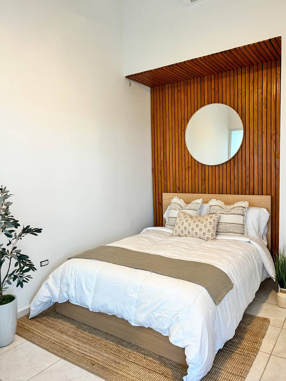 A bedroom with a full-height pine slat wall behind the bed and a round mirror