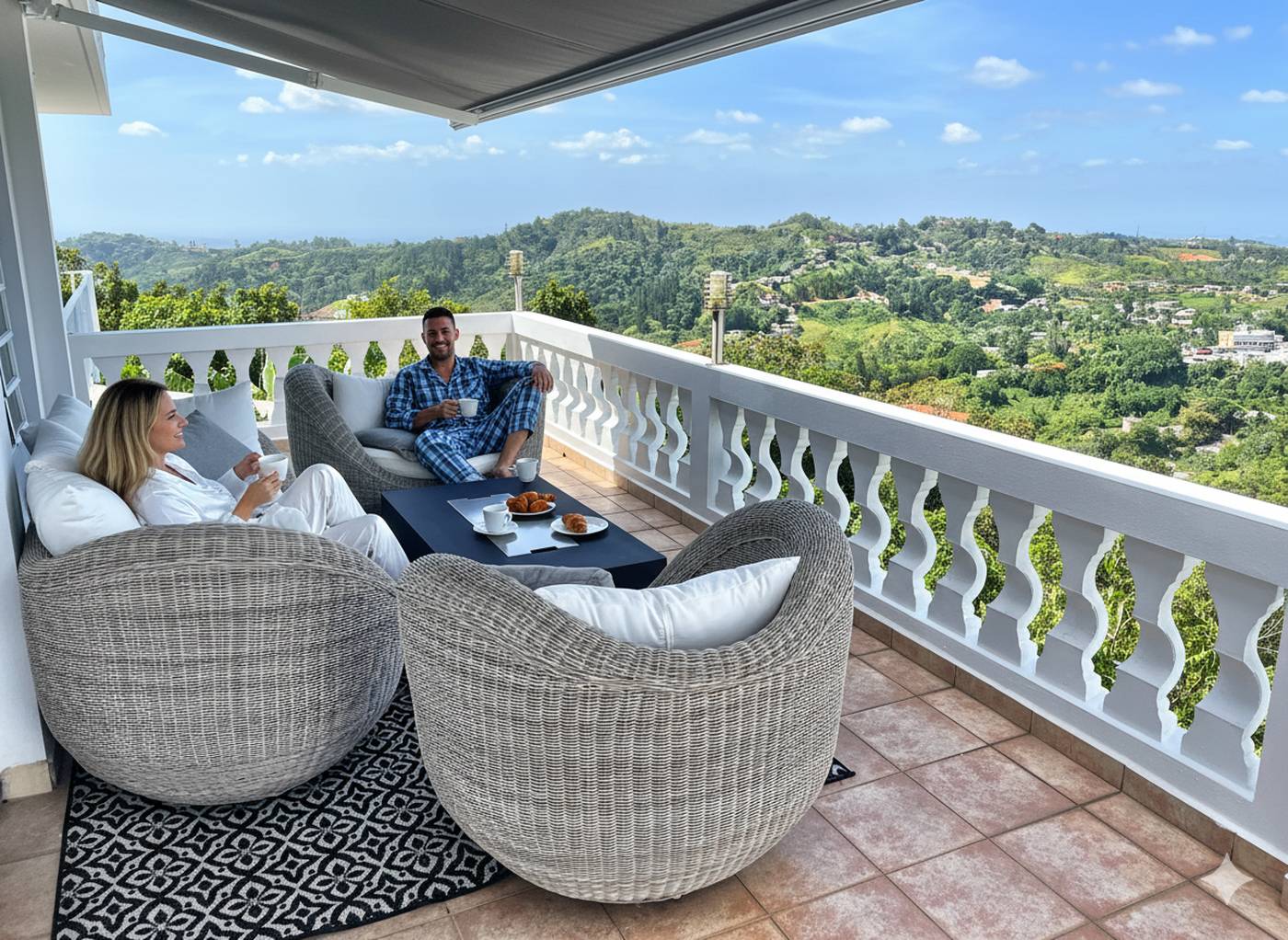 A couple having morning coffee in wicker chairs on the balcony, with the mountains beyond