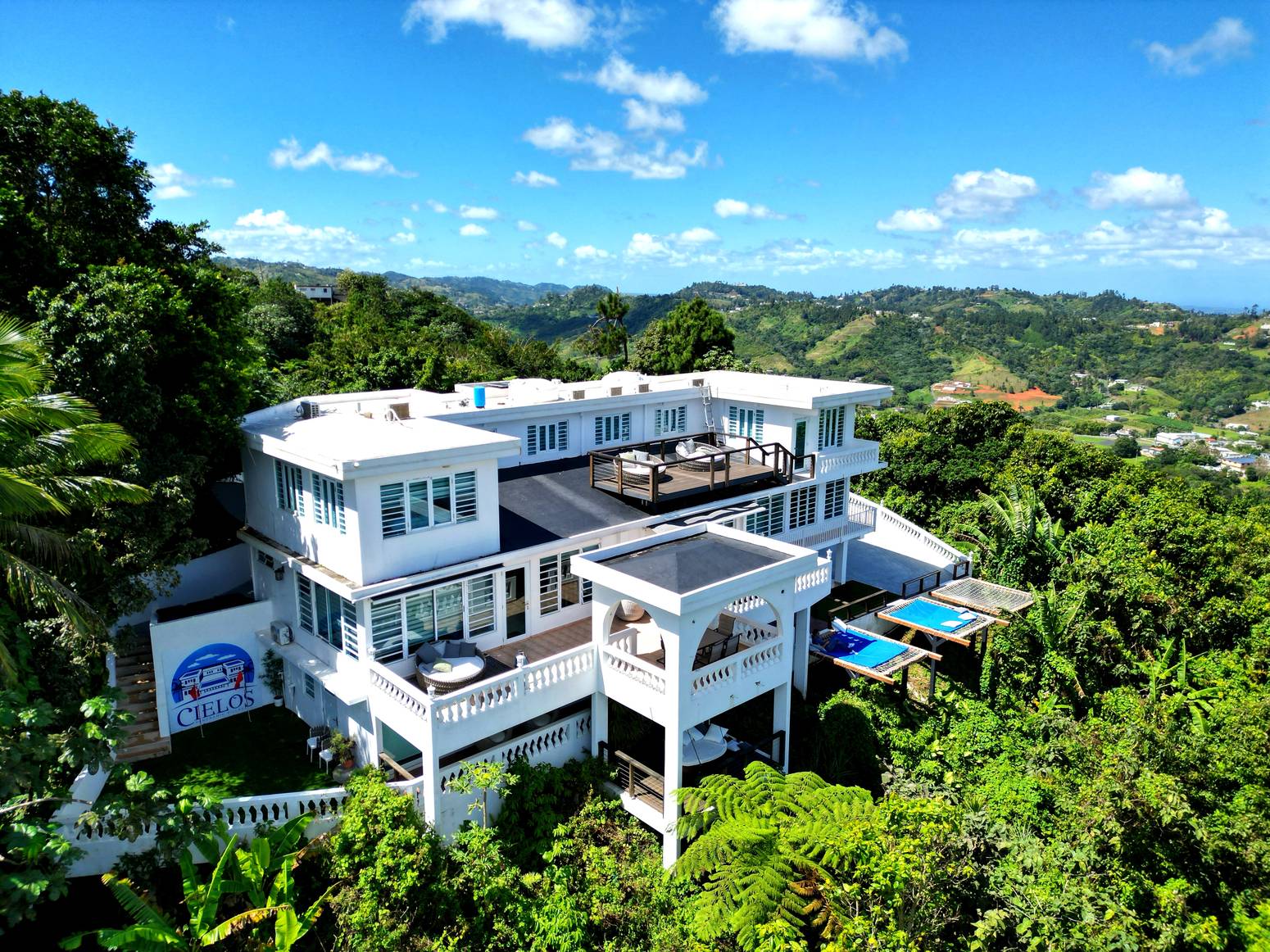 Aerial view of Cielos Panoramic Villas, a white estate on a green mountain ridge in Naranjito, Puerto Rico